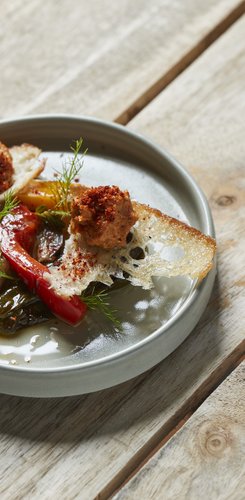 Ein Teller mit buntem Gemüse, knusprigem Brot und einer würzigen Paste, dekoriert mit frischen Kräutern auf einem Holztisch.