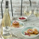 Eine Flasche Grau Burgunder steht neben zwei Gläsern Wein und zwei Tellern mit süßen, mit Puderzucker bestäubten Apfelküchlein.