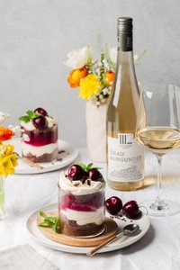 Zwei köstliche Dessertgläser mit Schichten aus Schokolade, Sahne und Kirschen, umgeben von bunten Blumen und einem Wein.