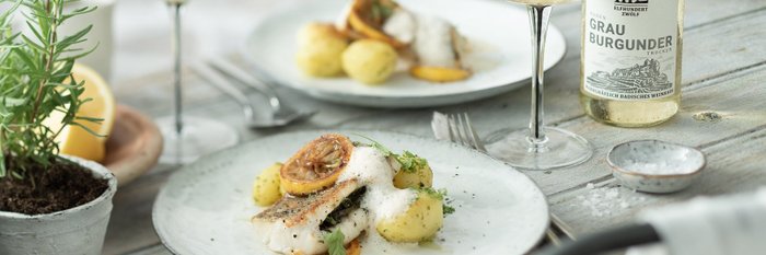 Ein elegantes Gericht mit gebratenem Fisch, Kartoffeln und Zitronenscheiben, serviert auf einem weißen Teller.